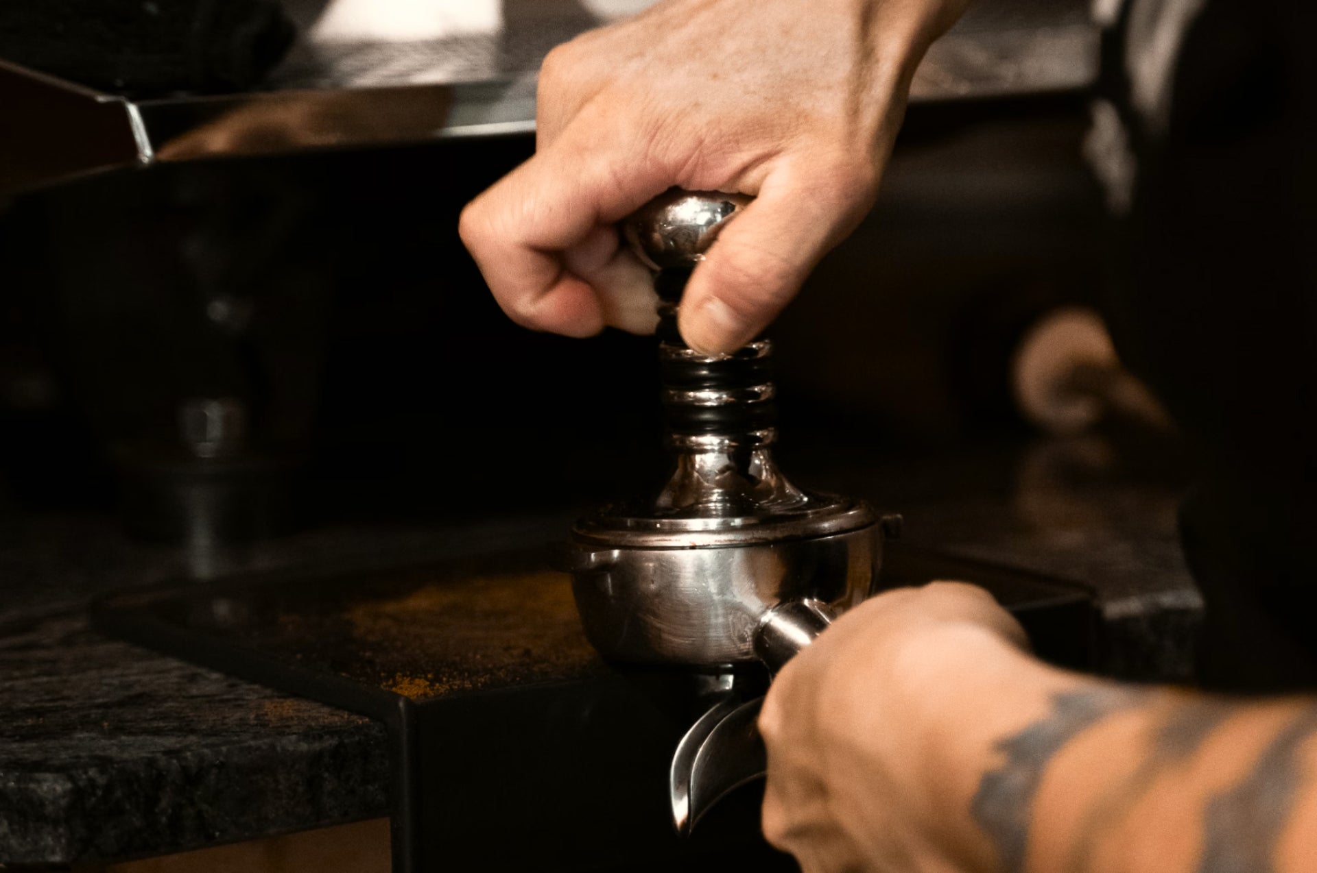Close up on a barista's hands while compressing grounded coffee into an espresso machine accessory