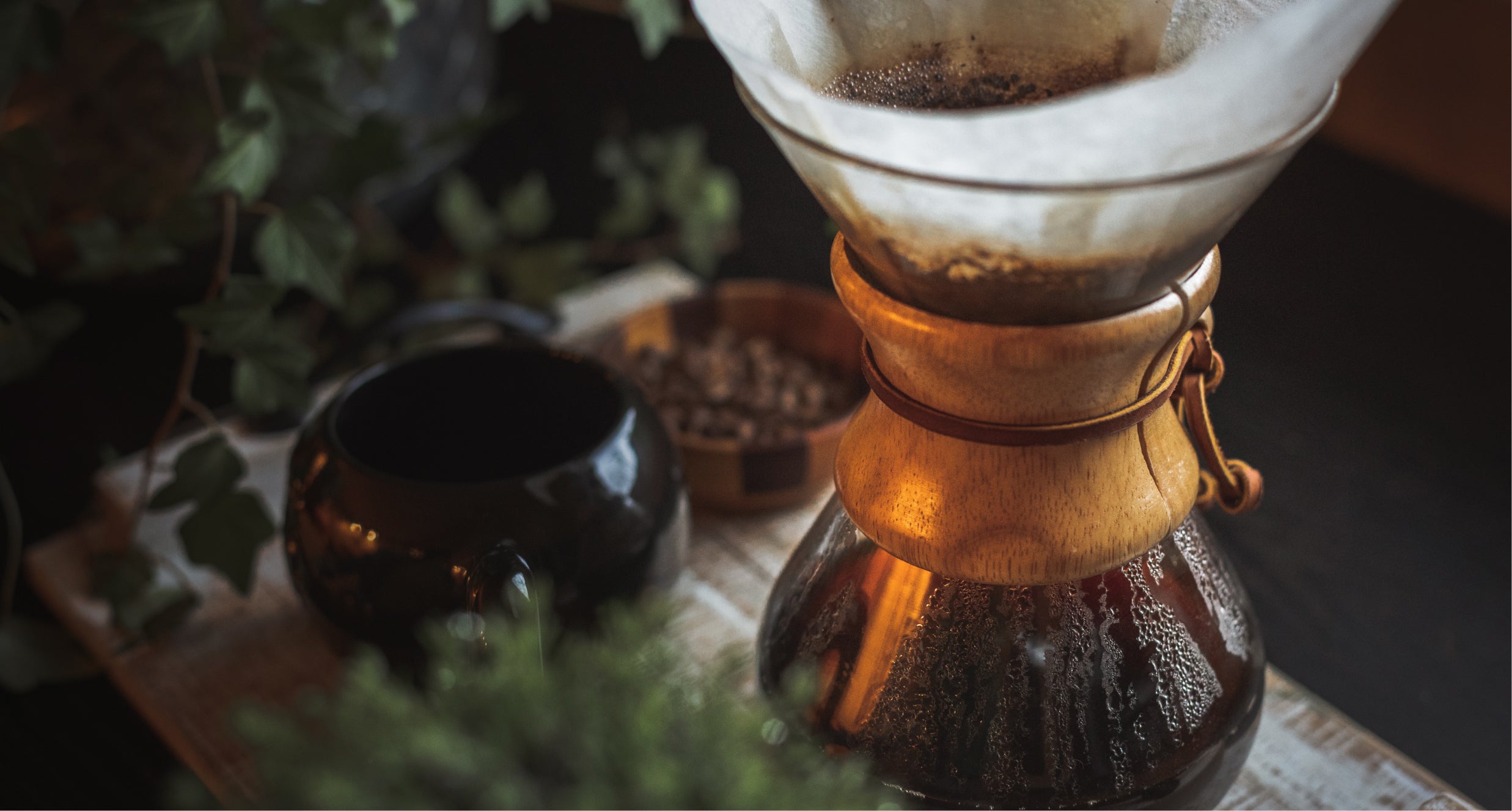 Chemex coffee maker brewing hot coffee on a table alongside other accessories